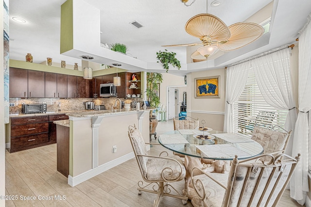 dining area with ceiling fan, sink, a towering ceiling, and light hardwood / wood-style floors