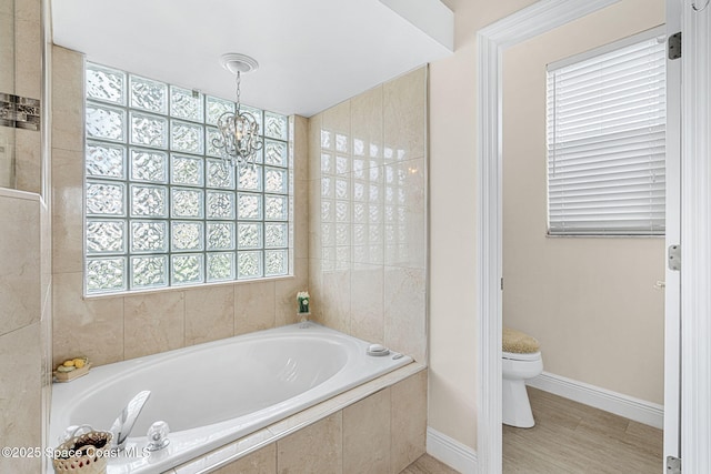 bathroom featuring a relaxing tiled tub, toilet, and a notable chandelier