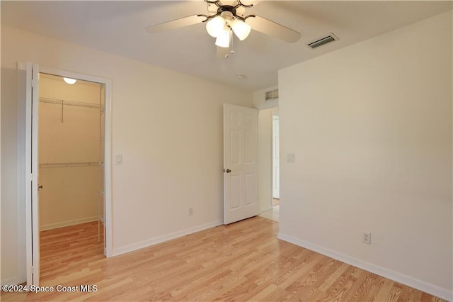 unfurnished bedroom with a walk in closet, ceiling fan, a closet, and light hardwood / wood-style floors