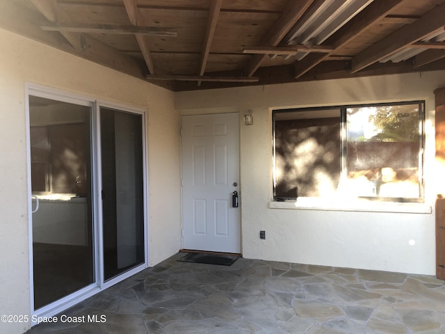 view of exterior entry with stucco siding and a patio area