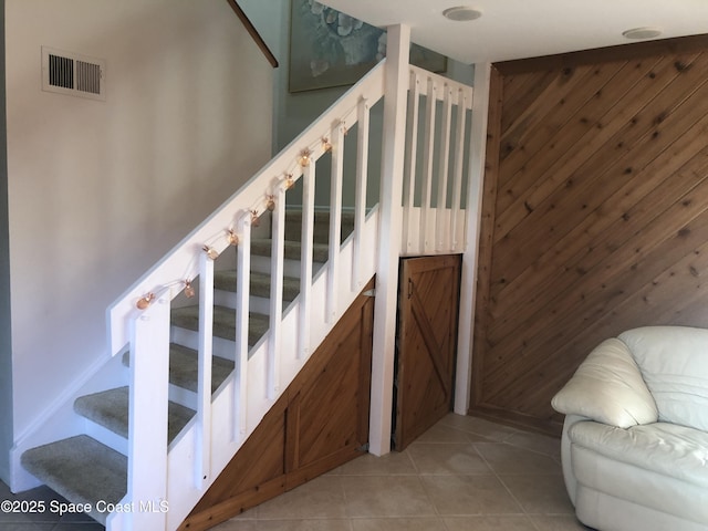 staircase with tile patterned floors, visible vents, and wood walls