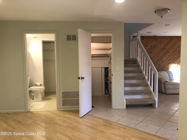 staircase with wooden walls, wood finished floors, and visible vents