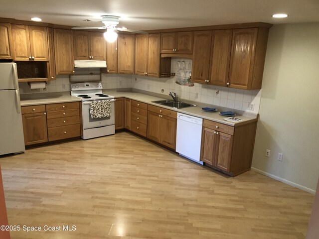 kitchen featuring under cabinet range hood, white appliances, brown cabinets, and a sink