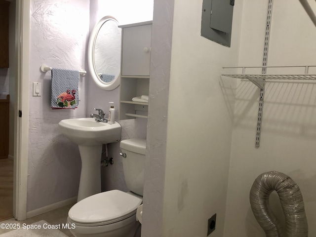 half bath featuring electric panel, toilet, baseboards, and a textured wall