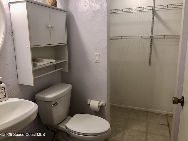 bathroom featuring toilet, baseboards, and a textured wall