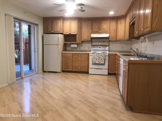 kitchen with white appliances, a sink, under cabinet range hood, tasteful backsplash, and brown cabinets