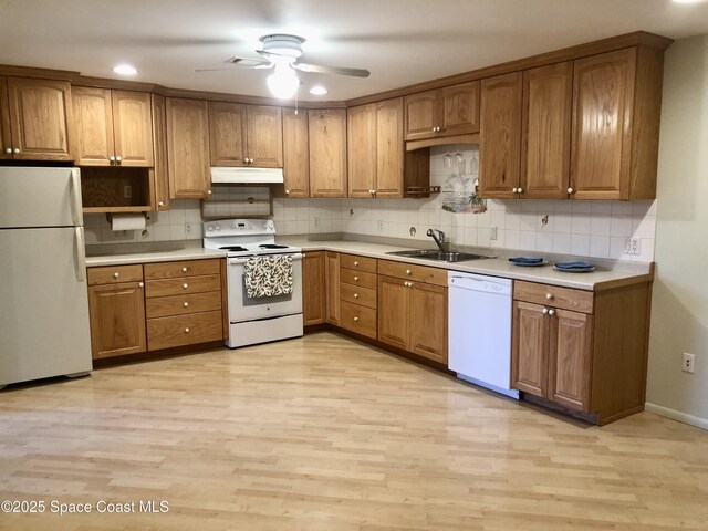 kitchen featuring under cabinet range hood, white appliances, brown cabinetry, and a sink