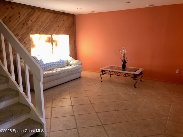 unfurnished living room featuring tile patterned floors, stairway, and wood walls