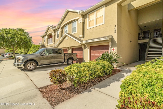 property exterior at dusk featuring driveway, a garage, stairs, and stucco siding