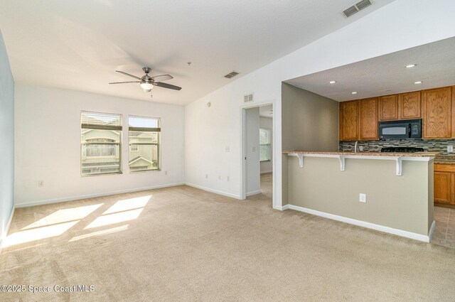 kitchen with black microwave, open floor plan, visible vents, and brown cabinets