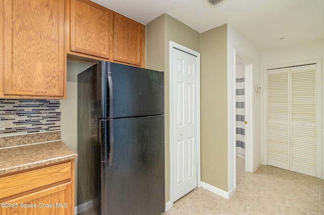 kitchen featuring baseboards, decorative backsplash, and freestanding refrigerator