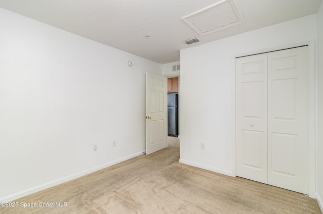 unfurnished bedroom with light carpet, visible vents, baseboards, freestanding refrigerator, and attic access