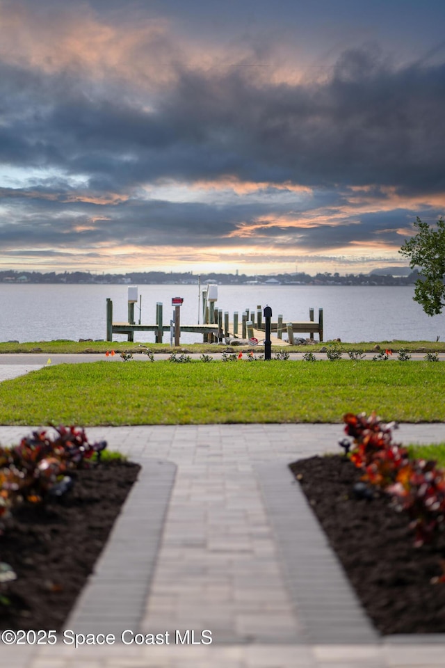 view of community featuring a boat dock, a yard, and a water view