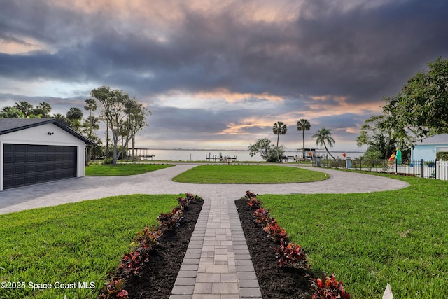 yard at dusk with a water view, a garage, and an outdoor structure