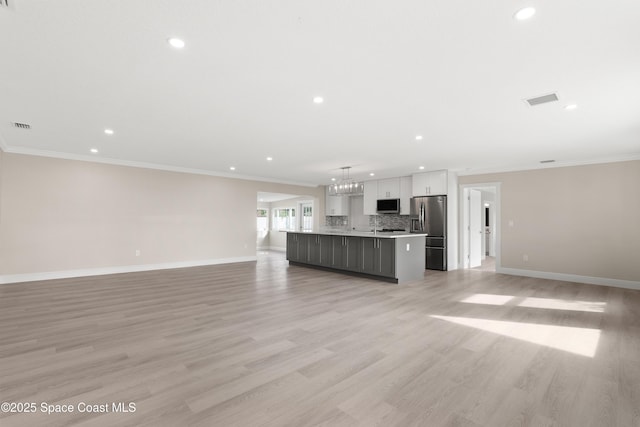 unfurnished living room with light hardwood / wood-style floors, ornamental molding, and an inviting chandelier