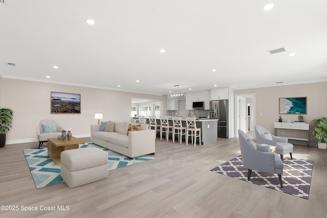 living room with a chandelier, light hardwood / wood-style floors, and crown molding