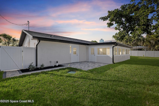 back house at dusk with a sunroom, a patio area, and a yard