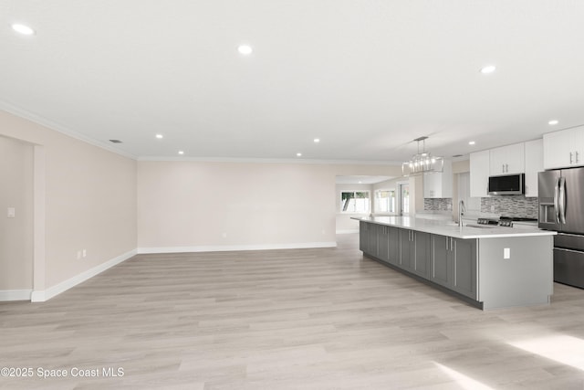 kitchen with stainless steel appliances, pendant lighting, light hardwood / wood-style flooring, white cabinetry, and an island with sink