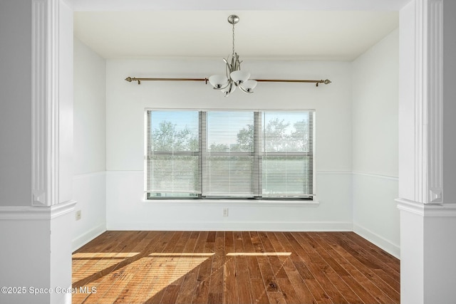 unfurnished dining area with decorative columns, a chandelier, and dark wood-type flooring