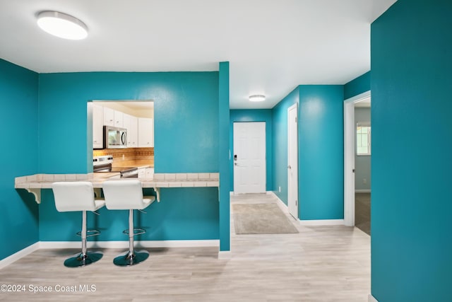 kitchen featuring tile countertops, a breakfast bar, white cabinets, and stainless steel appliances