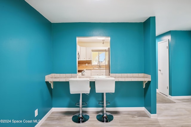 kitchen featuring white cabinetry, sink, backsplash, tile countertops, and a breakfast bar area