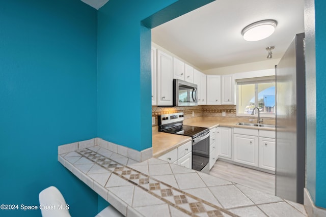 kitchen featuring tile countertops, white cabinets, sink, decorative backsplash, and appliances with stainless steel finishes