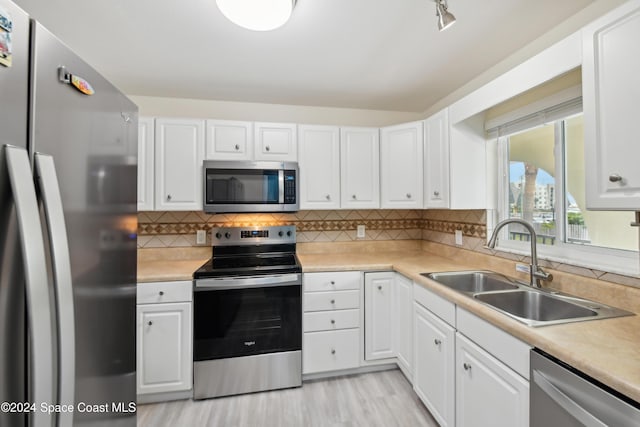 kitchen with appliances with stainless steel finishes, backsplash, sink, light hardwood / wood-style flooring, and white cabinetry