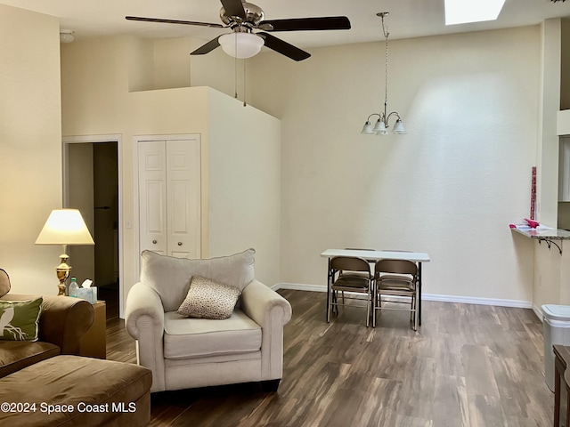 sitting room with ceiling fan with notable chandelier, dark wood-style floors, and baseboards