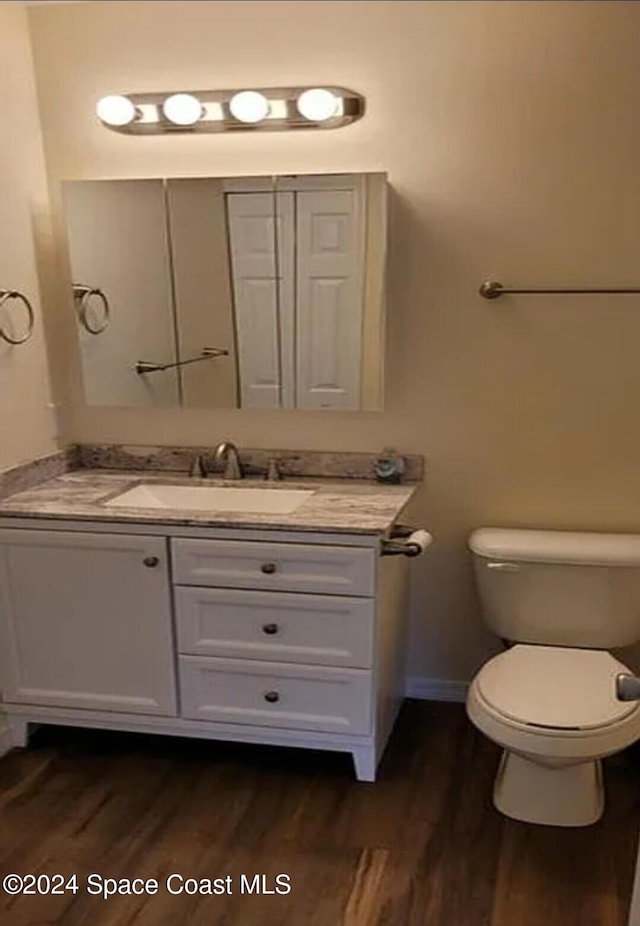 bathroom with baseboards, toilet, wood finished floors, and vanity