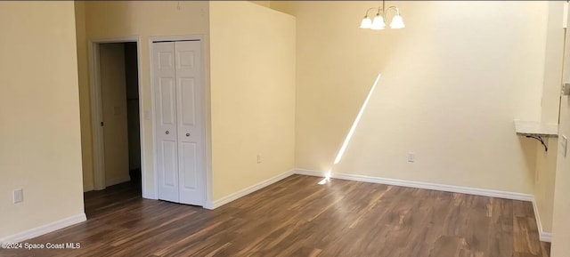 spare room with dark wood-style floors, an inviting chandelier, and baseboards