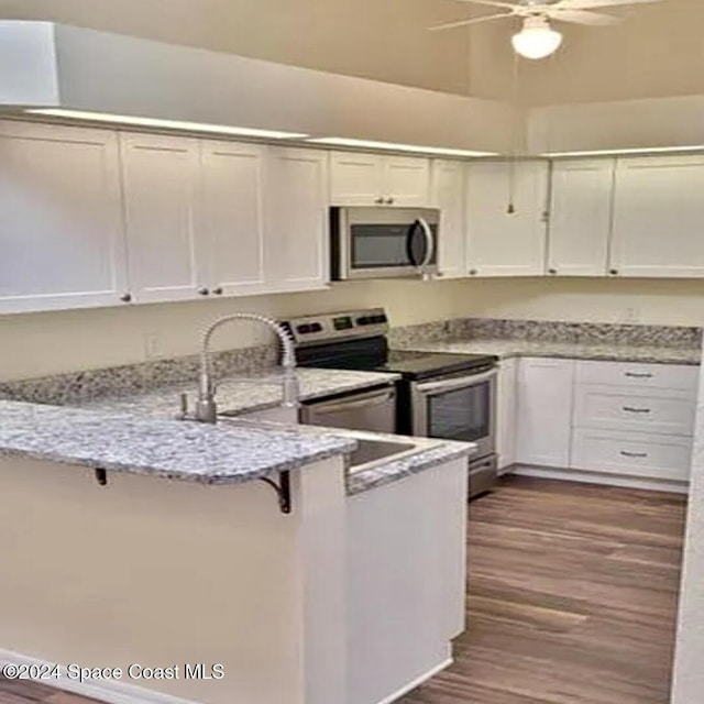 kitchen with light stone counters, a kitchen breakfast bar, stainless steel appliances, a peninsula, and dark wood-style flooring