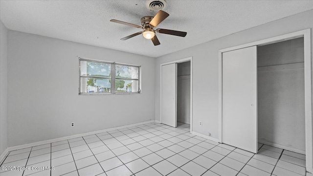 unfurnished bedroom featuring ceiling fan, light tile patterned flooring, a textured ceiling, and multiple closets