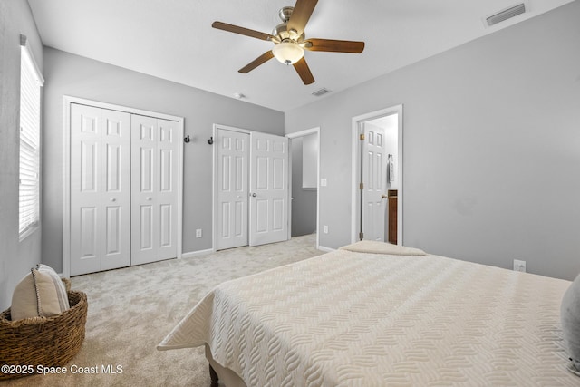 bedroom with ceiling fan, light carpet, and two closets