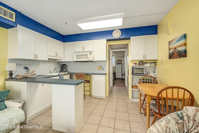 kitchen featuring backsplash, kitchen peninsula, light tile patterned floors, white cabinetry, and a breakfast bar area