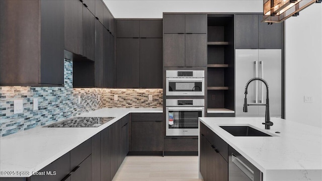 kitchen featuring backsplash, black electric stovetop, sink, light stone countertops, and double oven