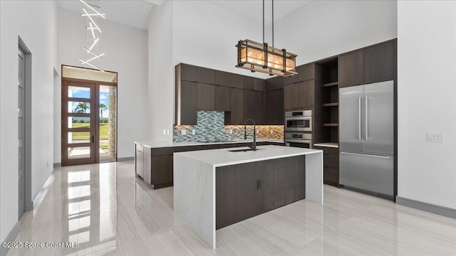 kitchen with french doors, stainless steel appliances, backsplash, pendant lighting, and a kitchen island with sink