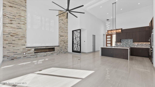 kitchen featuring backsplash, dark brown cabinets, decorative light fixtures, high vaulted ceiling, and a tiled fireplace