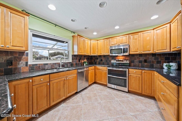 kitchen with light tile patterned flooring, stainless steel appliances, dark stone countertops, and sink