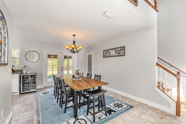 tiled dining room with a notable chandelier, a textured ceiling, beverage cooler, and french doors