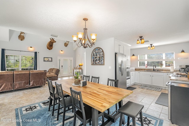 tiled dining space featuring a textured ceiling, plenty of natural light, a notable chandelier, and sink