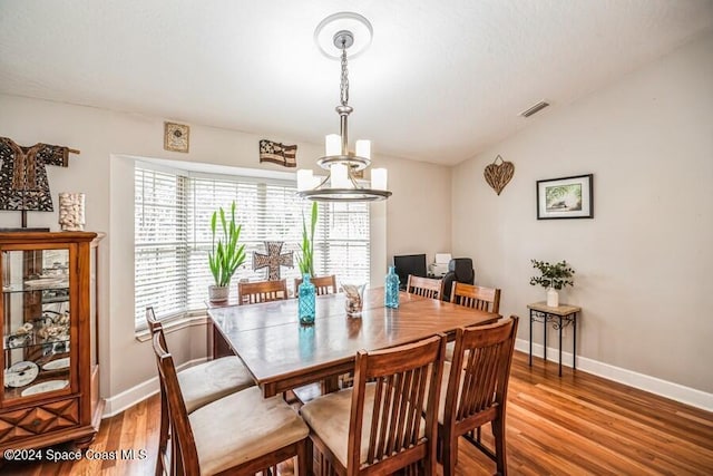 dining room with a chandelier, light hardwood / wood-style flooring, and lofted ceiling