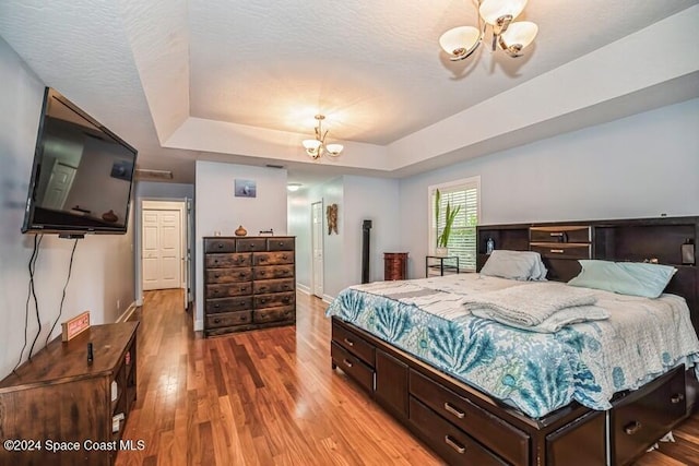 bedroom featuring hardwood / wood-style floors, a raised ceiling, and a notable chandelier