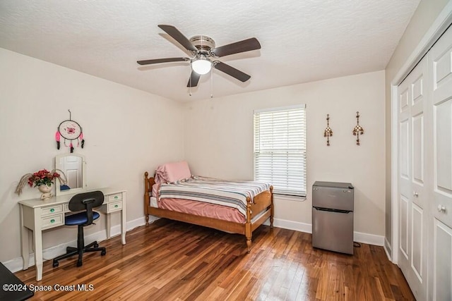 bedroom with stainless steel refrigerator, dark hardwood / wood-style flooring, ceiling fan, and a closet