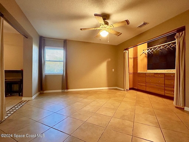 unfurnished bedroom with a textured ceiling, a closet, ceiling fan, and light tile patterned flooring