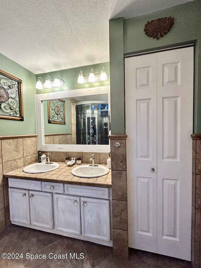 bathroom featuring a textured ceiling, vanity, and tile walls