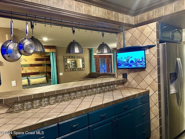 interior space with stainless steel fridge with ice dispenser, blue cabinets, tile counters, and crown molding