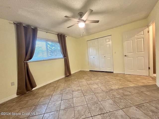 unfurnished bedroom featuring ceiling fan, a closet, light tile patterned floors, and a textured ceiling