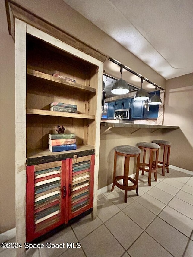 bar with blue cabinetry, light tile patterned flooring, and pendant lighting