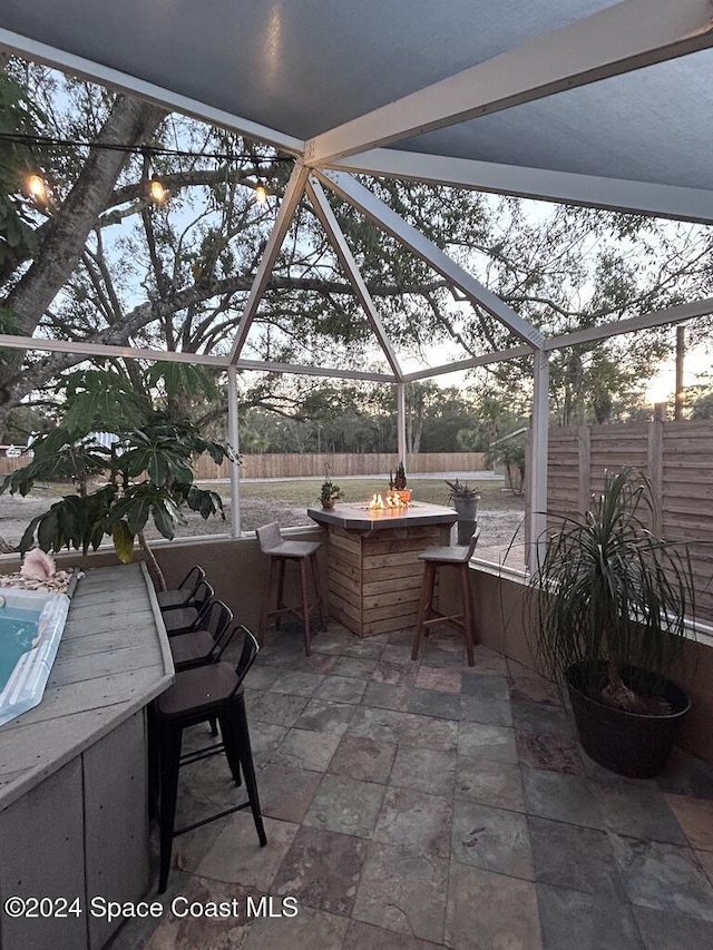 patio terrace at dusk with exterior bar, a fire pit, and a lanai