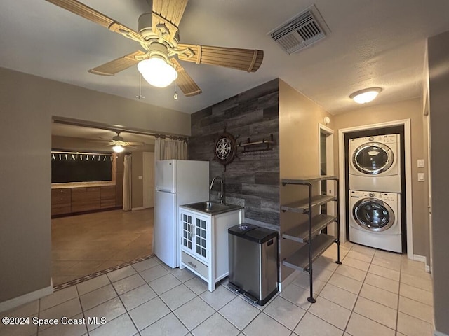 kitchen with ceiling fan, sink, stacked washer / dryer, white fridge, and light tile patterned floors